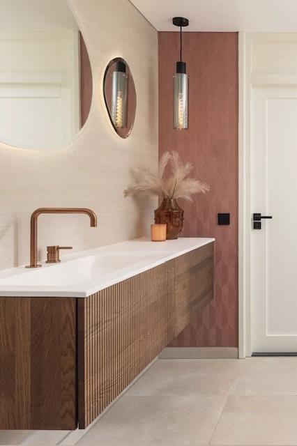 Moderne badkamer met houten wastafelmeubel, ronde spiegel en roze wand met verlichting