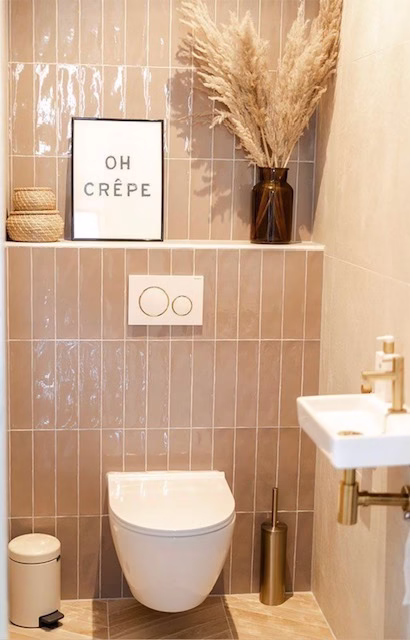 Moderne toiletruimte met beige wandtegels, hangtoilet, kleine wastafel en gouden details