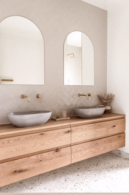 Moderne badkamer met houten wastafelmeubel, grijze waskommen, goudkleurige kranen en terrazzo vloer